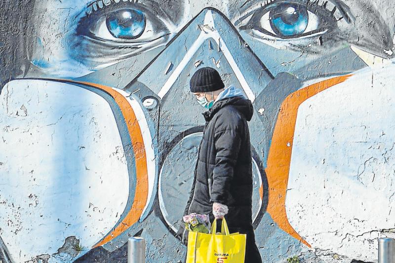 Un hombre portando un tapabocas camina por la calle en Milán, Italia, y al fondo se aprecia un mural alusivo a la protección de la pandemia del COVID-19.