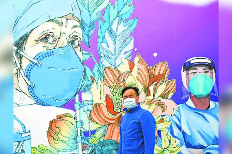 Un transeúnte con tapabocas camina frente a un mural en honor a los trabajadores de la salud en la ciudad china de Wuhan en la provincia de Hubei, foco de la pandemia.
